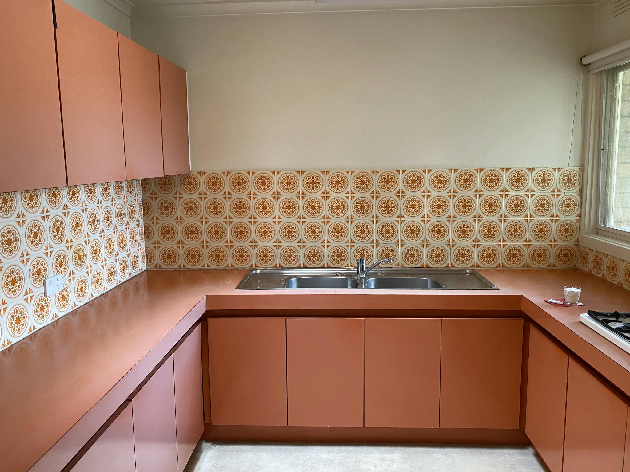 Retro kitchen design featuring orange cabinets and vintage patterned tiles.
